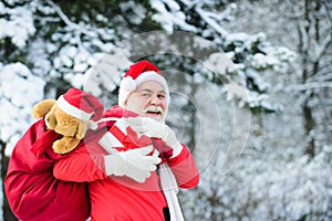 Funny Santa with Gift on Christmas Eve outside on fir snowy branch background.