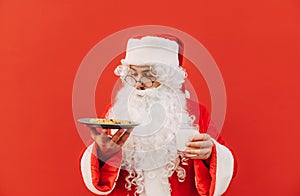 Funny santa isolated on red background with a glass of milk and a plate of chocolate chip cookies. Christmas and New Year concept