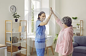 Funny and satisfied senior woman gives high five to young nurse who visited her at home.