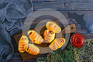 Funny sausage mummies in dough with ketchup on table. Halloween food. Top view. Flat lay