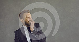 Funny scared businessman biting nails and looking to the side at copy space background