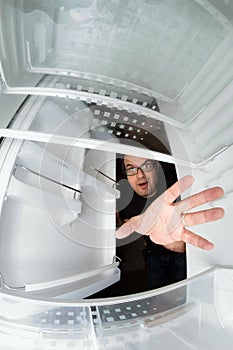 Funny scene of hungry young man opening the door of the fridge