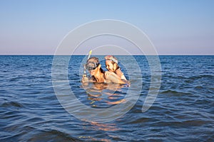 Funny scene with woman and little girl piggybacking with diving glasses in the water of a beach in Andalusia