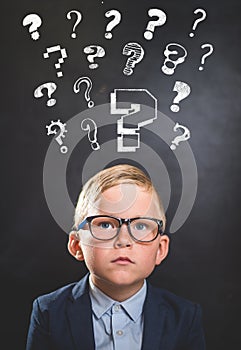 Funny school child with many question marks on blackboard. Little genius