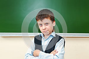 Funny schoolboy near the green school board in the classroom