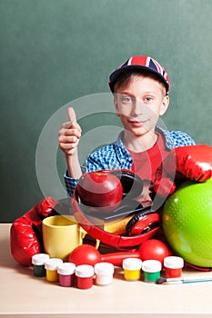 Funny schoolboy sitting at table with colorful school accessories