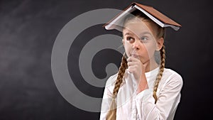 Funny schoolgirl with book on head planning homework schedule, education concept