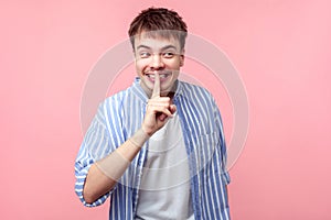 Funny secret, don`t tell anyone! Portrait of positive brown-haired man showing silence gesture.  on pink background