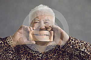 Funny senior man covering face with mobile phone with magnified picture of perfect smile