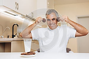 Funny senior man holding biscuits near the face and smiling with teeth. Crazy faces concept. Man fooling around and