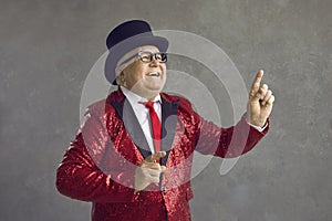 Funny senior man in retro party outfit dancing and having fun on gray studio background