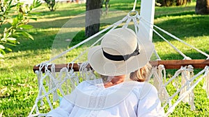 funny senior woman in a straw hat smiling happy relaxing on a hammock enjoying the fresh air on the terrace around the