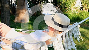 funny senior woman in a straw hat smiling happy relaxing on a hammock enjoying the fresh air on the terrace around the