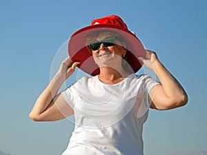 Funny senior woman wearing santa claus hat over sun hat on the sea beach, woman dancing and wishes a merry Christmas and happy new