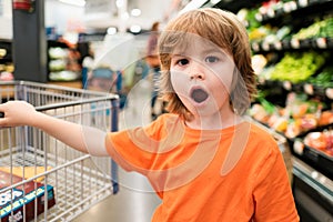 Funny shopping. Joyful beautiful child boy in supermarket buys vegetables. Healthy food for children.