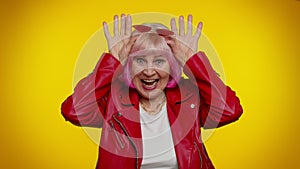 Funny silly senior old granny woman smiling friendly and doing bunny ears gesture on head, fooling