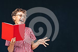 Funny smiling boy with glasses and book in his hand, posing on black background