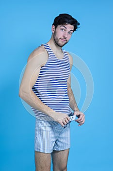 Funny Smiling Caucasian Handsome Brunet Man in Striped Underware Pulling Pants While Looking Aside Against Seamless Blue