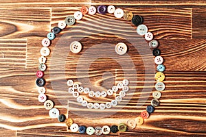 Funny smiling face shape made with sewing buttons to wooden background.