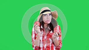 funny, smiling female farmer in checkered shirt and hat, holding in hands two large sour apples, eats, bites them