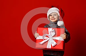 Funny smiling joyful child boy in Santa red hat holding Christmas gift present in hands