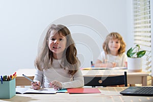 Funny smiling kids in classroom at school. Schoolboy and schoolgirl sitting at desk and writing a text.