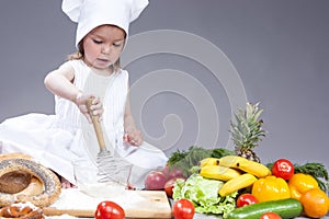 Funny Smiling Little Caucasian Girl In Cook Uniform Making a Mix of Flour, Eggs and Vegetables