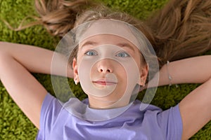Portrait of funny smiling little girl lying on green carpet