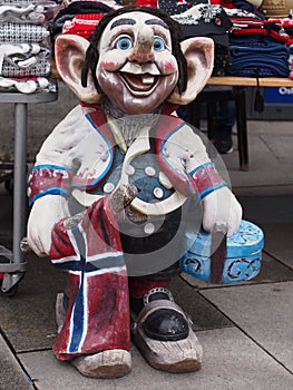 Funny smiling troll statue toothless holding Norwegian flag and gift box at the entrance of a gift shop in Norway