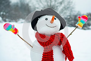 Funny snowman in stylish hat and scarf on snowy field. The morning before Christmas. Funny snowmen. Snowman with a bag