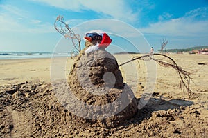 Funny Snowman in Sunglasses and Santa Red Hat, made of the Sand on Goa beach