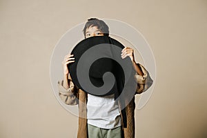 Funny spooked indian boy in oversize long sleeve shirt hiding behind pole hat