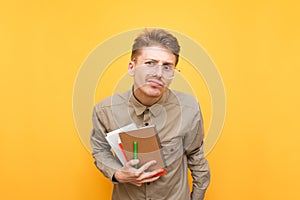 Funny student in glasses,shirt and with books and exercise books in hands, surprised looking at the camera. Surprised nerd stands