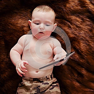 Funny surprised baby boy with a phone in his hands on a fur carpet. Curious child holds a smartphone, top view