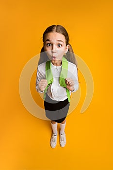 Funny Surprised Schoolgirl Looking At Camera Standing On Yellow Background