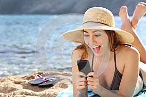 Funny surprised woman watching social media in a smart phone on the beach photo