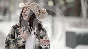 Funny teen girl is singing song outdoor at city at winter day, listening to music by smartphone