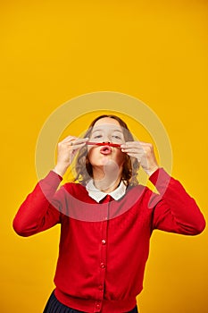 Funny teen school girl make mustache on her face with red pencil,