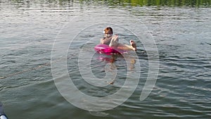 Funny teenage girl is sitting in scuba mask, life jacket on swimming circle in sea and holding on to rope. Dad rides his