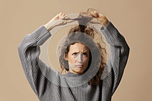 Funny thoughtful curly beautiful female in gray casual sweater with hairbrush comb pulls curls up posing isolated on
