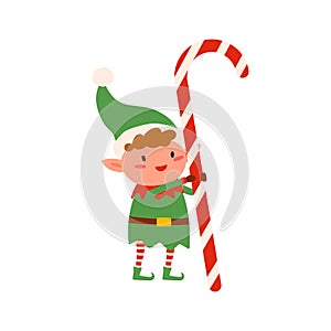 Funny tiny elf in green costume holding huge Christmas candy cane vector flat illustration. Cute Santa helper holding