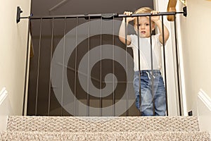 Funny toddler approaching safety gate of stairs