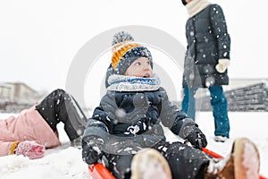 Funny toddler boy and his big sisters having fun with a sleigh in beautiful winter park. Cute child playing in a snow