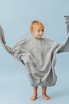 Funny toddler boy swinging sleeves of huge oversized grey thick warm shirt