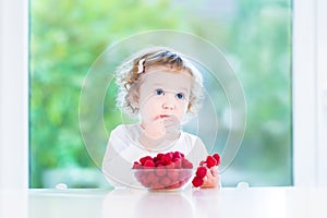 Funny toddler girl eating raspberries at white table