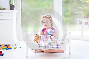 Funny toddler girl feeding her toy bear in sunny room