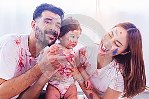 Funny toddler girl get stain color by put to faces and body with happy family, laughing together. Caucasian father and Asian