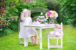 Funny toddler girl playing tea party with a doll