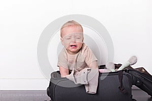 Funny toddler sitting in the suitcase and trying to pack it. Cute baby boy going to vacation