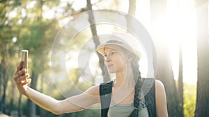 Funny tourist girl in hat taking selfie photos with smartphone camera during travelling and hitchhiking